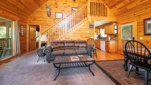 A log cabin interior with a wooden staircase, a sofa, a coffee table, and a dining area. - Hot Tub & Game Room: Log Cabin 2 Mi to Ripley’s! (Gatlinburg)