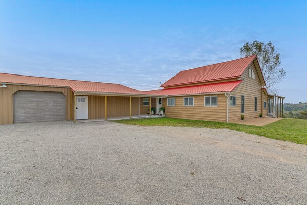 Une maison à deux étages avec un toit rouge, un garage et une véranda à l’avant.