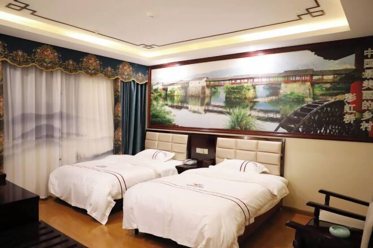 A hotel room with two beds, a large mural of a bridge over water, and a traditional Chinese design on the ceiling.