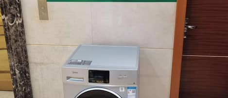 A commercial laundry machine with a digital display, located in a hallway with a marble floor and a wooden door.