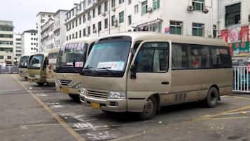 Una fila de minibuses color beige estacionados en un estacionamiento, con edificios al fondo.