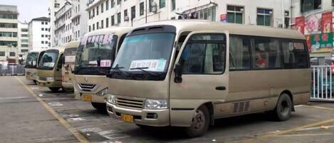 A row of beige minibuses parked in a lot with buildings in the background.