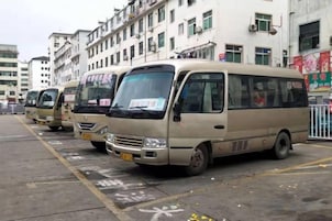 Uma fileira de micro-ônibus bege estacionados em um estacionamento, com edifícios ao fundo.