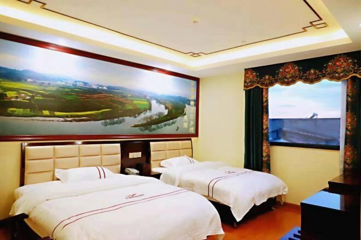 A hotel room with two beds, a large TV screen, a desk, and a window with curtains.