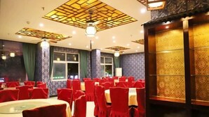 A banquet hall with round tables and red chairs, featuring patterned wallpaper and a decorative ceiling.
