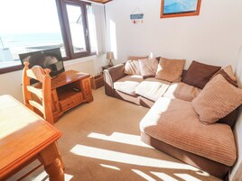 Una sala de estar acogedora con un sofá, un mueble de televisión de madera, una mesa y vistas al mar a través de un ventanal amplio.