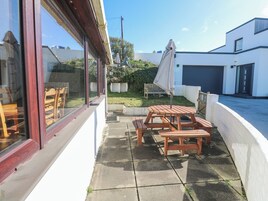 Un patio con mesas y bancos de madera, césped y un edificio blanco con garaje.