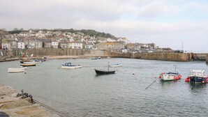 Un puerto con barcos, un muro de piedra y casas al fondo.
