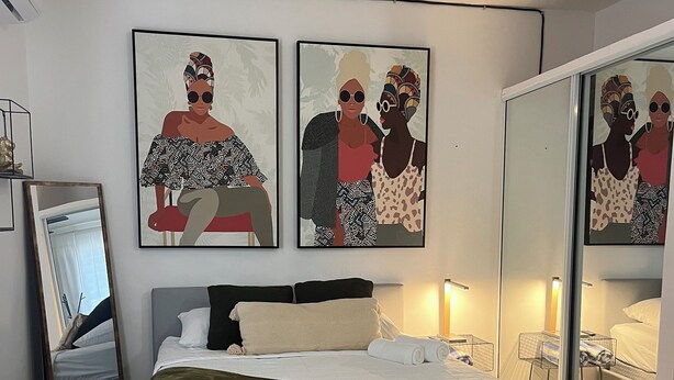 A modern bedroom with a large bed, a bedside table, a mirror, and artwork on the wall. - Vista Ramey Apartment (Aguadilla)