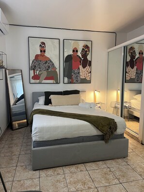 Une chambre à coucher moderne avec un grand lit, une table de chevet, un miroir et des œuvres d’art accrochées au mur.