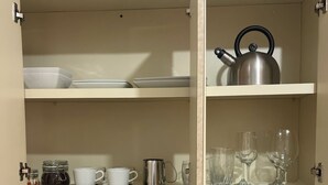 A kitchen with a stainless steel sink, a white microwave, and shelves with dishes, cups, and a kettle. - Vista Ramey Apartment (Aguadilla)