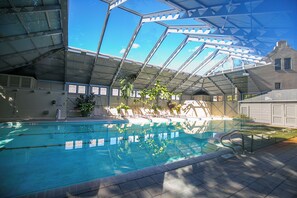 An indoor swimming pool with a glass ceiling, surrounded by lounge chairs and potted plants.