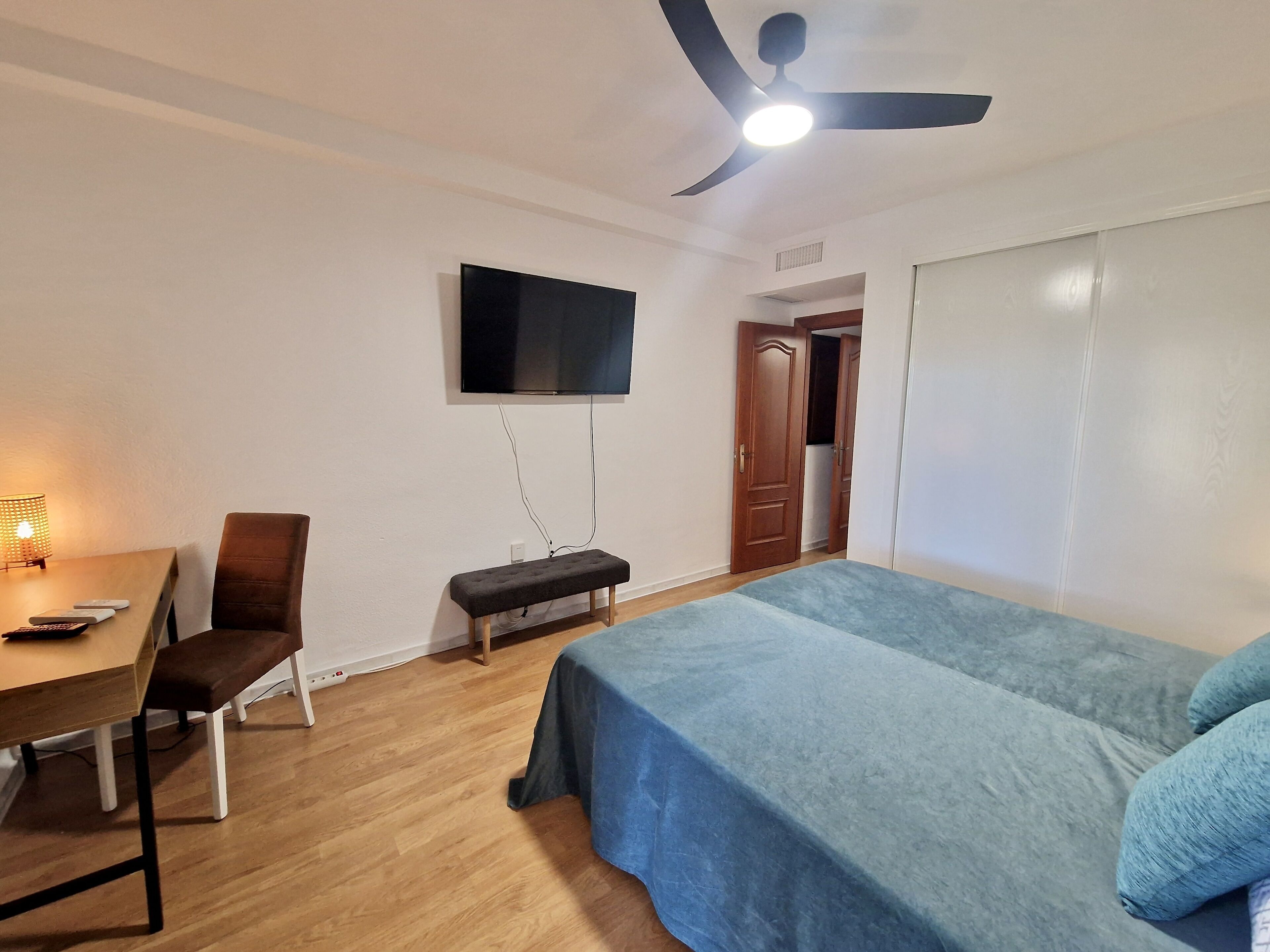 A bedroom with a bed, a desk, a chair, a television, and a ceiling fan.