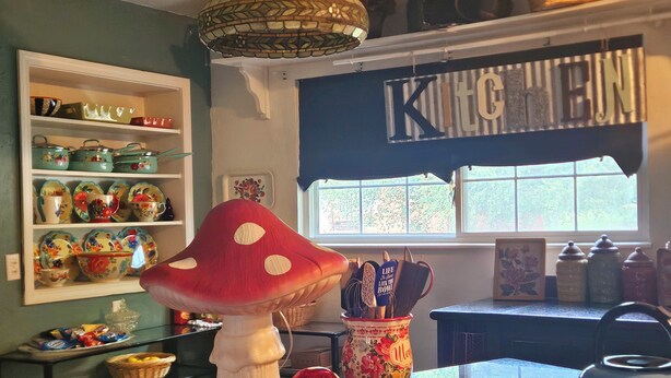 A kitchen with a large mushroom decoration, a shelf with colorful dishes, and a window with a view of greenery. - Whimsical 3 bd cottage for families and pets. Sleeps 7, free wifi/snacks (Midwest City)