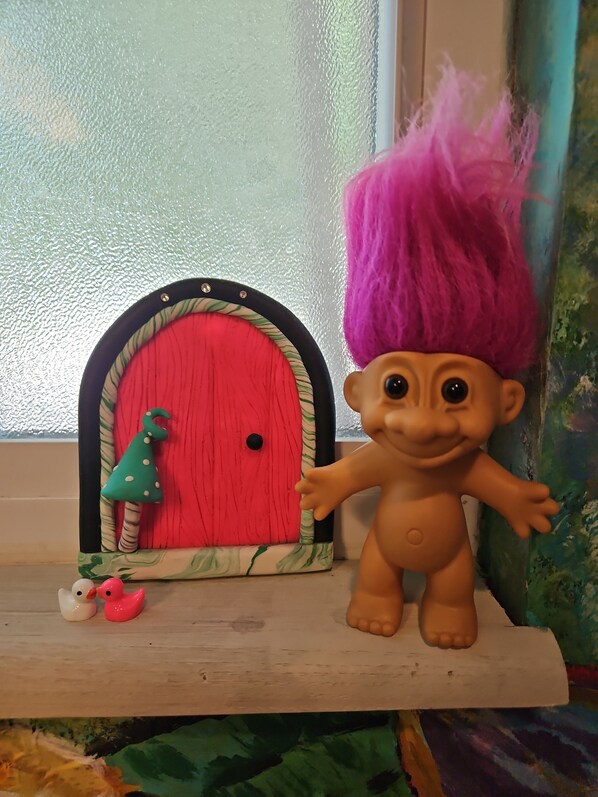 A doll with a pink mohawk next to a red door with a green and white frame.