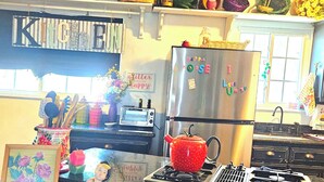 A kitchen with a stainless steel refrigerator, a red teapot, a toaster, and a sign that reads "HAPPY HOUSE." - Whimsical 3 bd cottage for families and pets. Sleeps 7, free wifi/snacks (Midwest City)