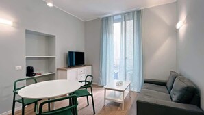 Un salon moderne avec une table ronde, des chaises vertes, un canapé, un téléviseur et une fenêtre avec des rideaux.