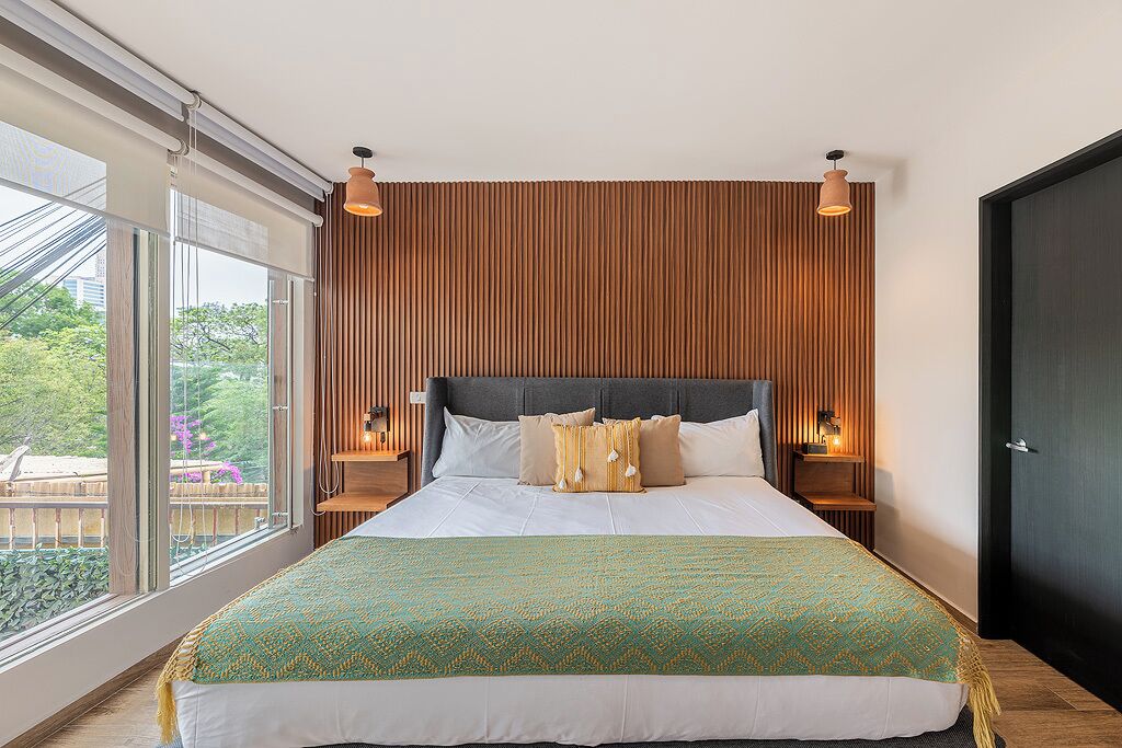 Un dormitorio moderno con una cama grande, un panel de pared de madera, dos lámparas de noche y vistas a zonas verdes al exterior.