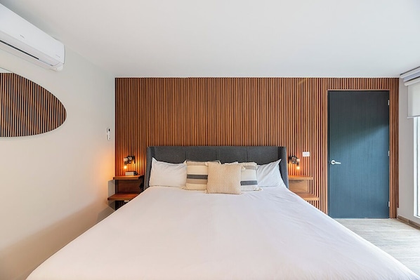 A modern hotel room with a large bed, wooden paneling on the walls, a dark door, and a small bedside table with a lamp. - Ciceron 612 Polanco (Mexico City)