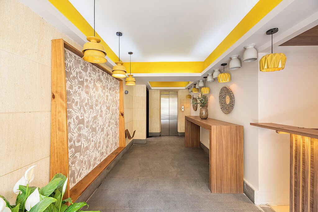 A modern hotel lobby with a wooden reception desk, patterned wallpaper, and a central elevator.