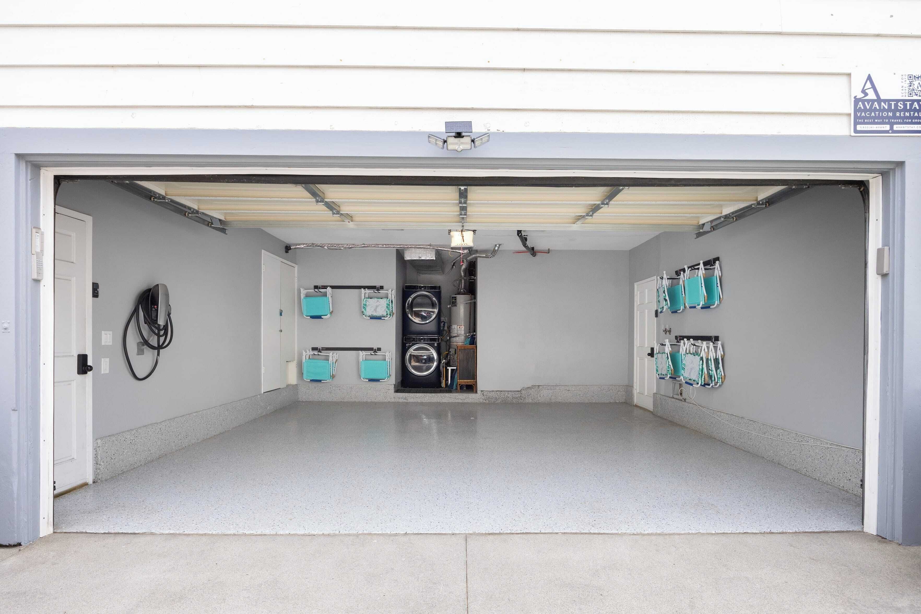 A garage with a clean, tiled floor and a closed garage door. There are several bags hanging on the wall, a washing machine, and a dryer visible inside.