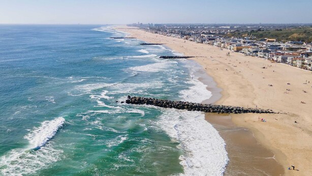 A coastal beach with a long pier extending into the ocean, a sandy beach with people, and a cityscape in the background. - Coastal-chic Newport Stay Steps to the Beach, Dining & Boardwalk Optional Add-on Unit (Newport Beach)