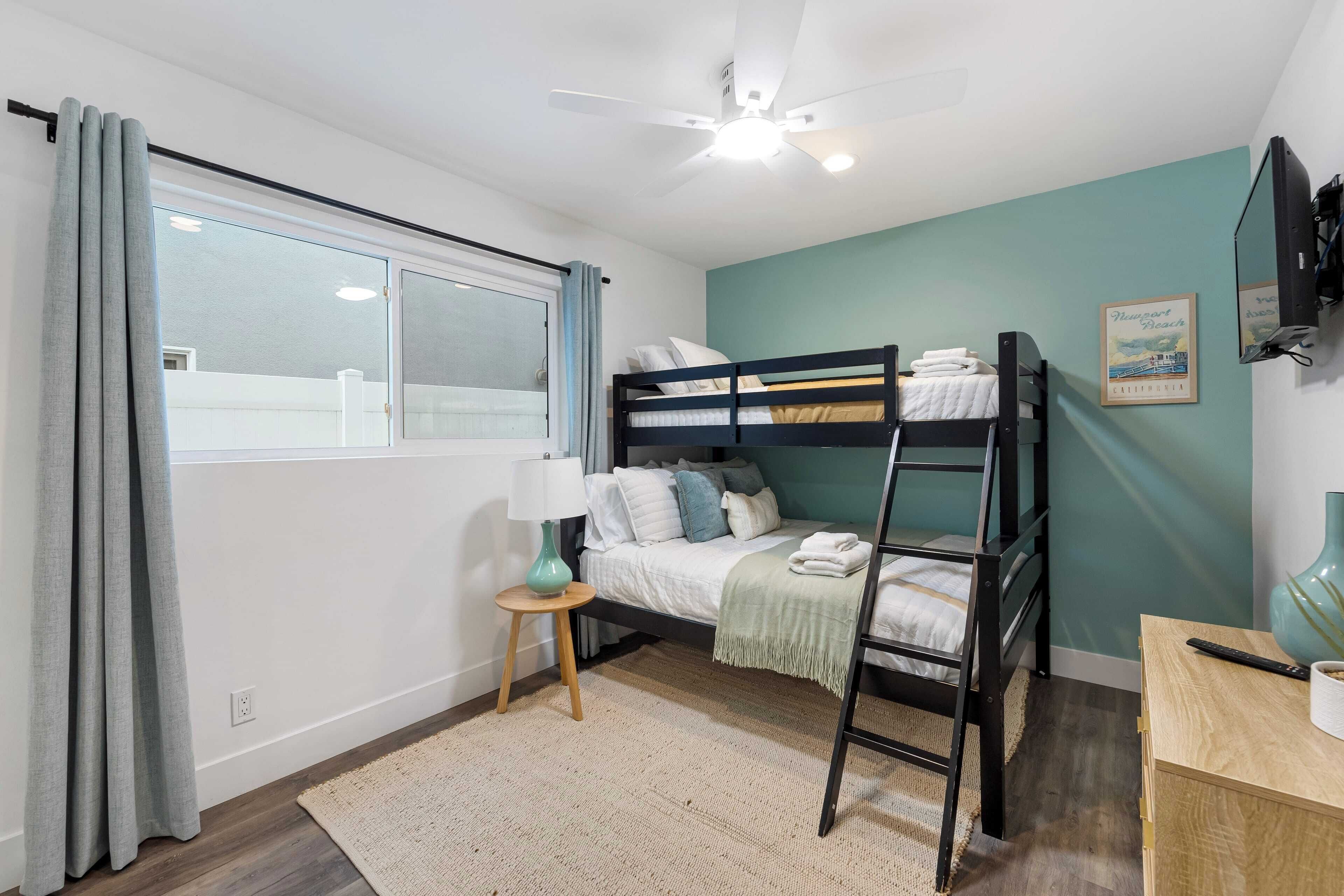 A bedroom with a bunk bed, a desk, a lamp, and a window with curtains.