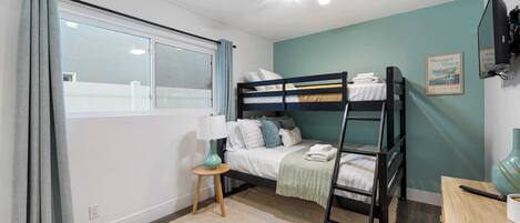 A bedroom with a bunk bed, a desk, a lamp, and a window with curtains.