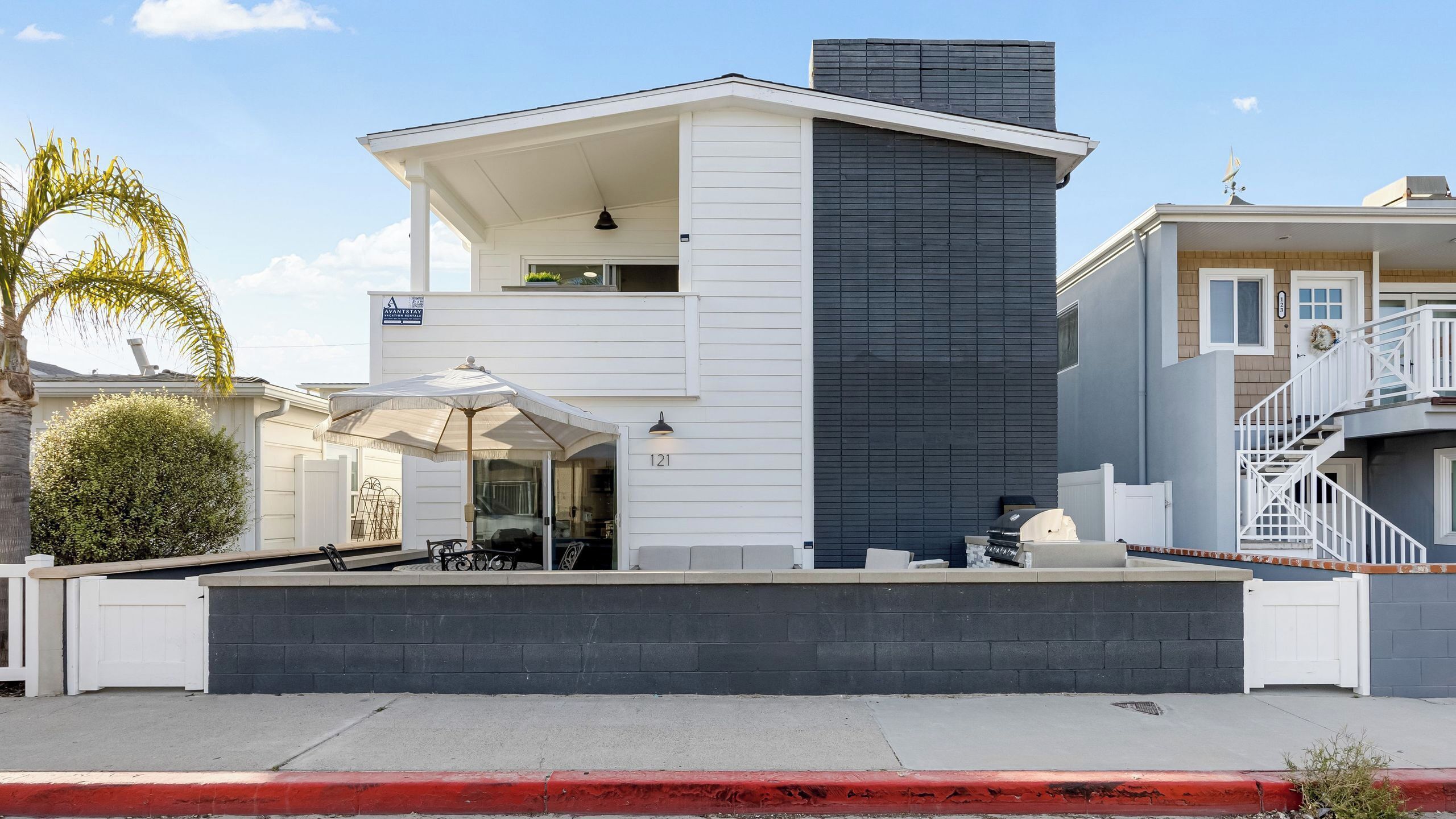 A modern two-story house with a covered patio, a black vertical facade, and a white exterior.