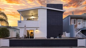 A two-story house with a balcony, a garage, and a covered outdoor seating area. - Coastal-chic Newport Stay Steps to the Beach, Dining & Boardwalk Optional Add-on Unit (Newport Beach)