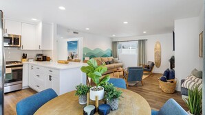 A modern apartment with a kitchen, dining area, and living room. It includes a stove, microwave, dining table, and sofas. - Coastal-chic Newport Stay Steps to the Beach, Dining & Boardwalk Optional Add-on Unit (Newport Beach)