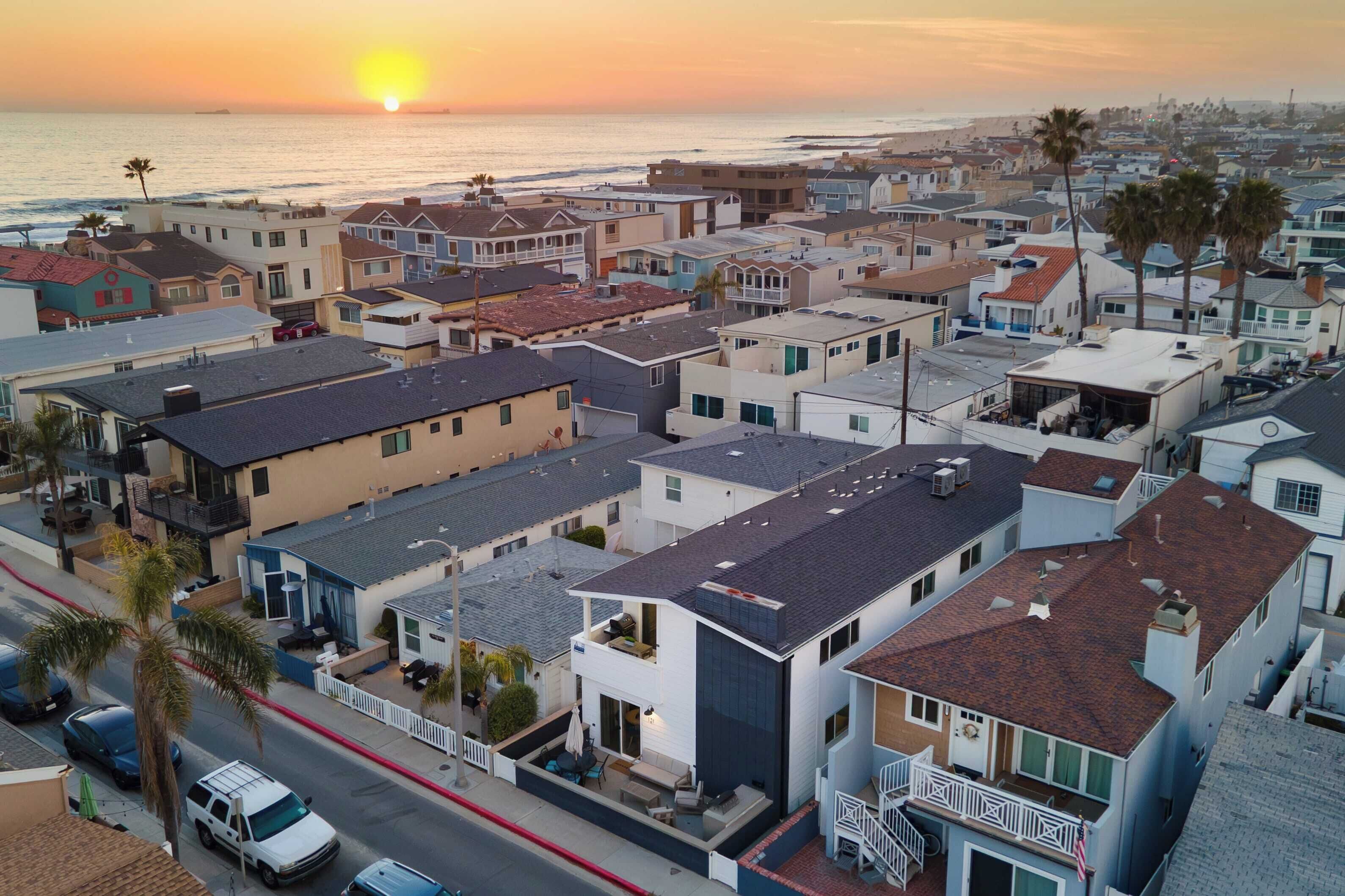 Una zona residencial costera con casas, algunas con balcones, y una puesta de sol sobre el océano.