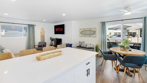 A modern living room with a white island, blue chairs, and a wooden dining table. - Coastal-chic Newport Stay Steps to the Beach, Dining & Boardwalk Optional Add-on Unit (Newport Beach)