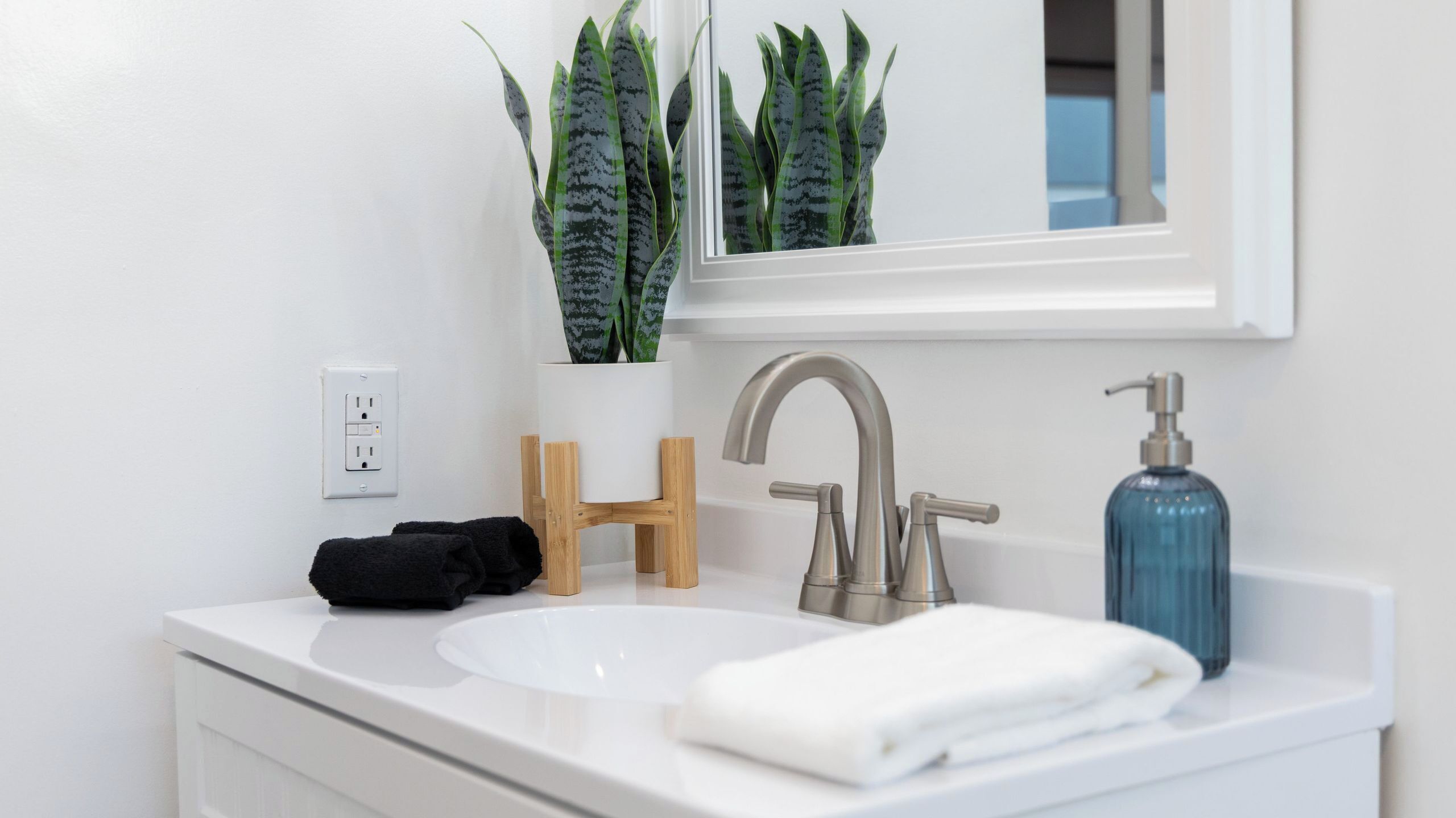 A white bathroom sink with a modern faucet, a blue soap dispenser, and a mirror above.