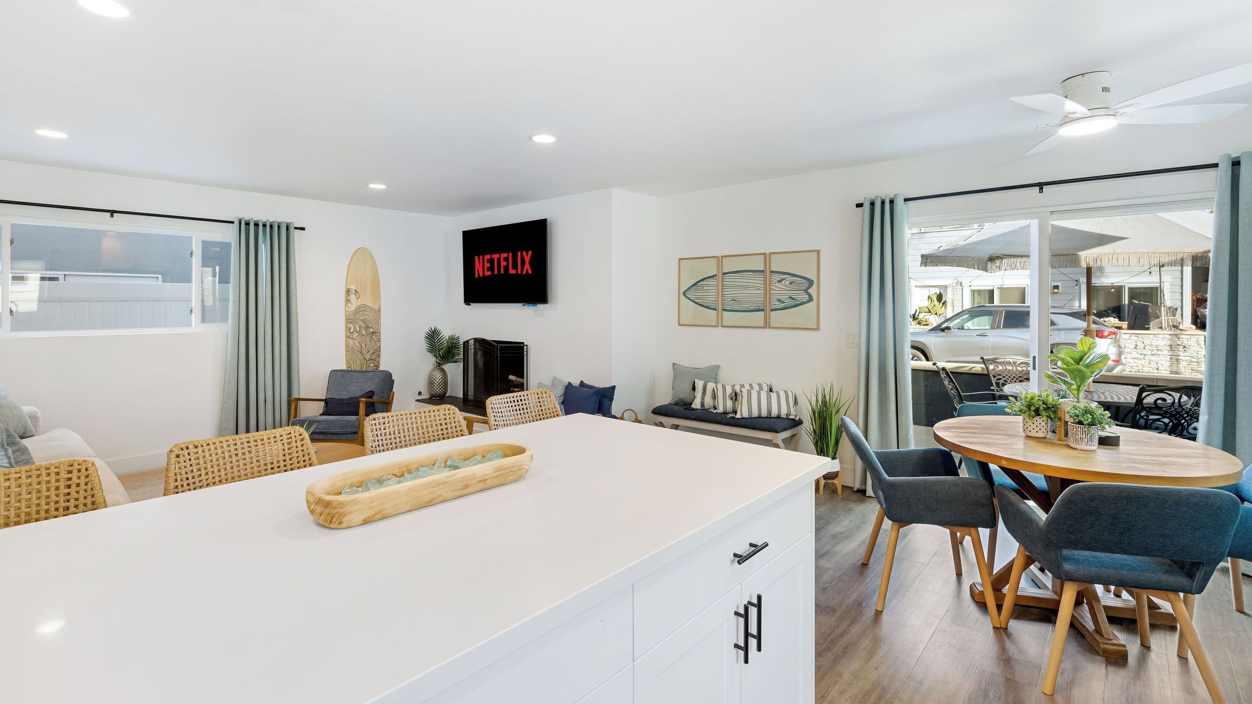 A modern living room with a white island, a flat-screen TV, and a dining area with a round table and chairs.