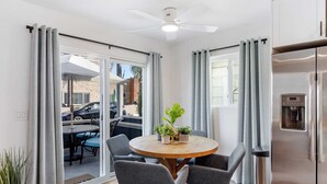 A modern kitchen with a stainless steel refrigerator, a round wooden table with four grey chairs, and a ceiling fan. - Coastal-chic Newport Stay Steps to the Beach, Dining & Boardwalk Optional Add-on Unit (Newport Beach)