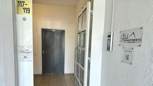 Un couloir avec une porte fermée, une pancarte indiquant les numéros d’appartements 117 à 119, et un code QR pour obtenir les coordonnées.