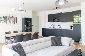 A modern living room with a sofa and chairs, a dining area with a table and chairs, and a kitchen with dark cabinets and appliances. - modern apartment,close to center with parking spot (Koblenz)