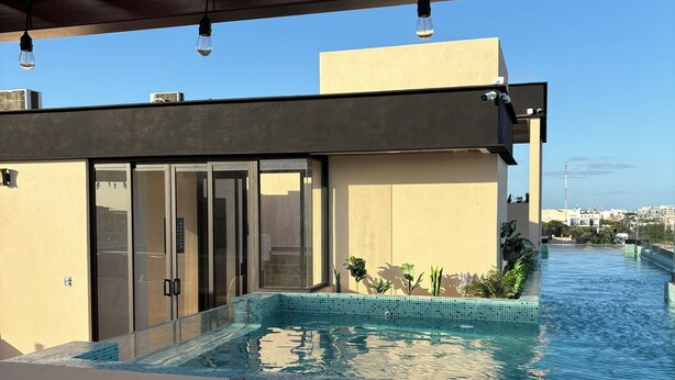 Ein moderner Außenpool mit Glaskante, einer Pergola darüber und blauem Himmel im Hintergrund.