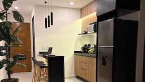 Eine moderne Küche mit Kühlschrank, Mikrowelle und Holzschränken. Es gibt einen Essbereich mit Tisch und Stühlen sowie einen Blumentopf.
