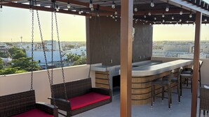 Eine Dachterrasse mit Korbsesseln, einer Bar und hängenden Lampen.