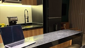 Eine moderne Küche mit integriertem Mikrowellenherd, einer Kaffeemaschine und einem Kühlschrank. Auf der Arbeitsfläche steht ein Laptop und es gibt vier Barhocker.
