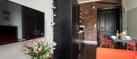 A modern living room with a flat-screen TV, a black entertainment unit, a vase of pink tulips, and a bright orange sofa.