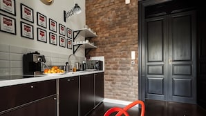 A modern kitchen with dark wooden cabinets, a white countertop, and a brick wall. There are framed certificates on the wall, a coffee machine, and a red chair in the foreground. - Cracow Fancy Brick #1 – Old Town (Kraków)