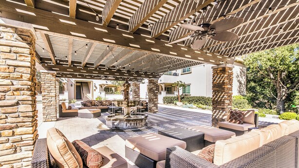 An outdoor patio with wicker furniture, a stone wall, and a fountain.