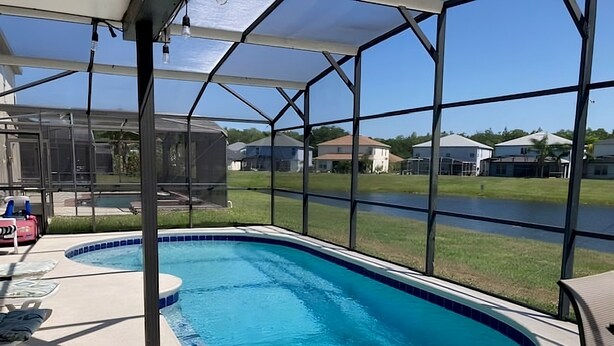 A swimming pool with a covered area, surrounded by houses and a clear sky. - Perfect Private Disney Vacation Getaway With Private Pool (Kissimmee)
