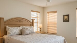 A bedroom with a large bed, a nightstand, a lamp, and two windows with blinds. - Perfect Private Disney Vacation Getaway With Private Pool (Kissimmee)