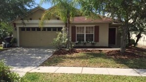 A single-story house with a garage, a front yard with a lawn, and a tree. - Perfect Private Disney Vacation Getaway With Private Pool (Kissimmee)