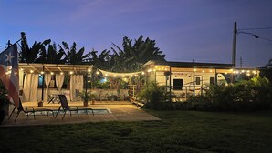 A well-lit RV with a covered patio area, surrounded by lush greenery and a flag. - El Camper with private pool (Maleza Alta)