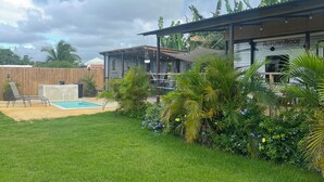 A backyard with a swimming pool, a covered patio, and lush greenery. - El Camper with private pool (Maleza Alta)